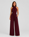 Woman wearing a halter neck wide leg jumpsuit with a defined waistband, flowing silhouette, sleeveless design, and elegant draped fabric for formal occasions.