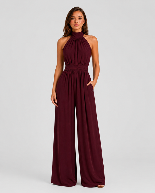 Woman wearing a halter neck wide leg jumpsuit with a defined waistband, flowing silhouette, sleeveless design, and elegant draped fabric for formal occasions.