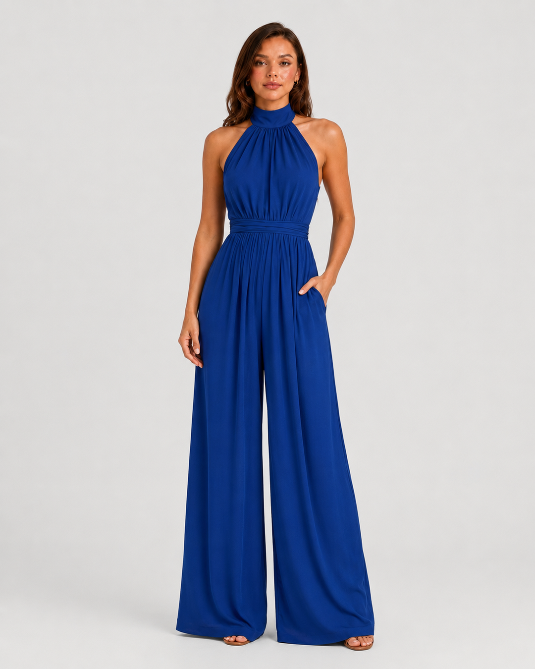 Woman wearing a halter neck wide leg jumpsuit with a defined waistband, flowing silhouette, sleeveless design, and elegant draped fabric for formal occasions.