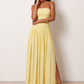 Woman wearing the Zofia strapless A-line maxi dress featuring a smocked square-neck bodice, shirred waist, flowing A-line skirt with a side slit, and a backless design.