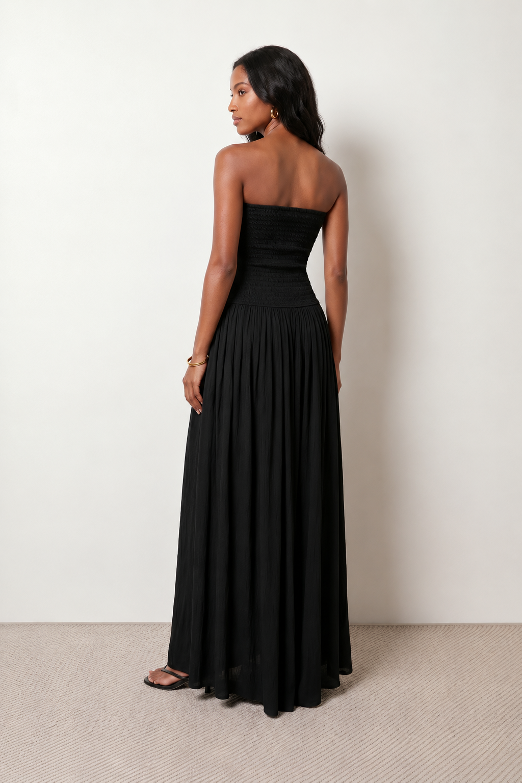 Woman wearing the Zofia strapless A-line maxi dress featuring a smocked square-neck bodice, shirred waist, flowing A-line skirt with a side slit, and a backless design.
