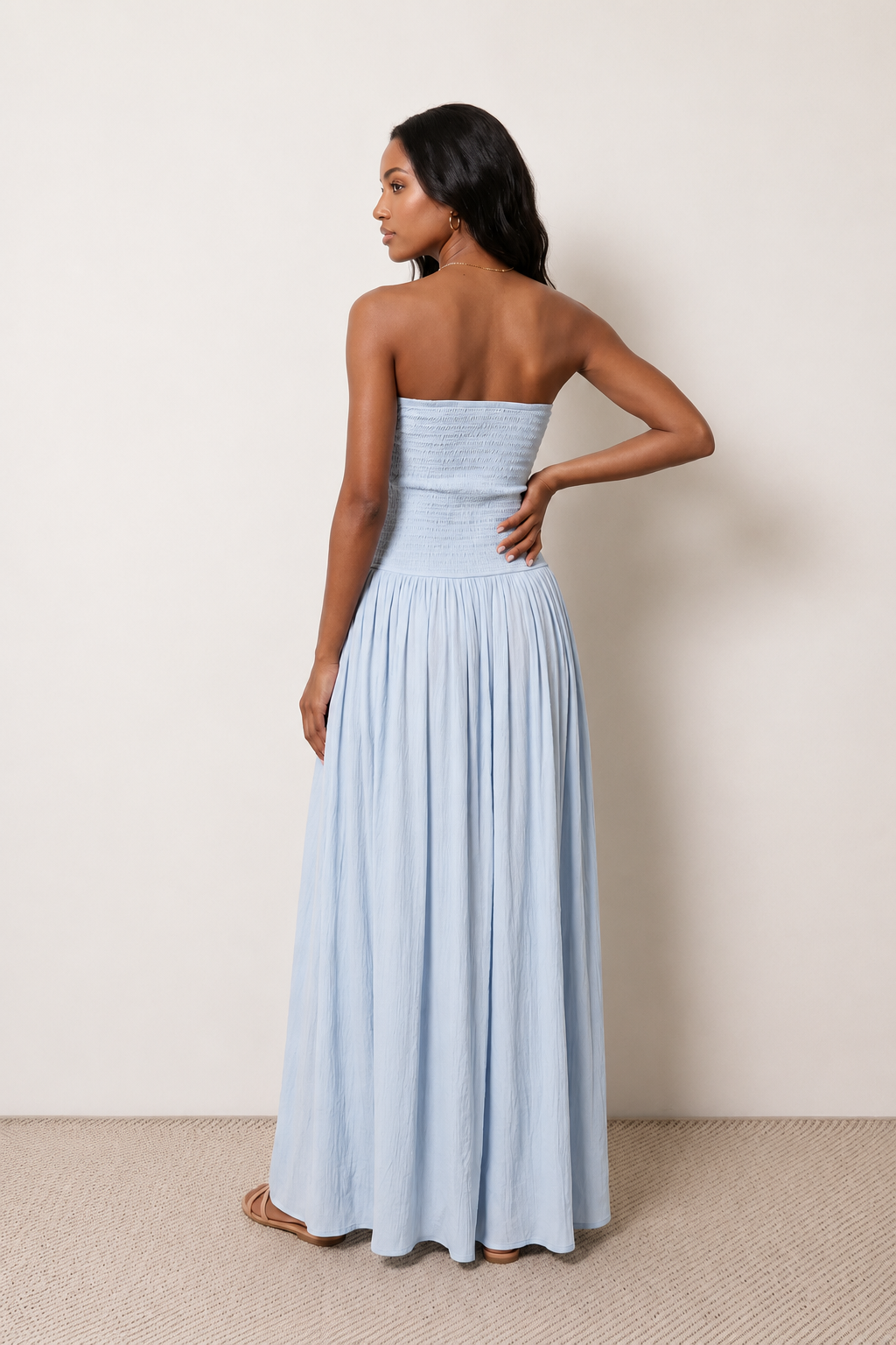 Woman wearing the Zofia strapless A-line maxi dress featuring a smocked square-neck bodice, shirred waist, flowing A-line skirt with a side slit, and a backless design.