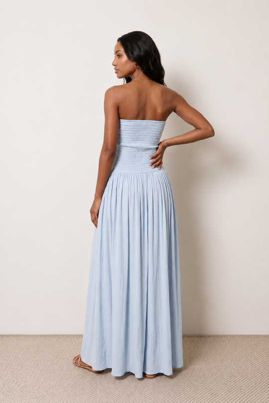 Woman wearing the Zofia strapless A-line maxi dress featuring a smocked square-neck bodice, shirred waist, flowing A-line skirt with a side slit, and a backless design.