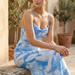 Seren spaghetti strap maxi dress in an abstract floral print featuring a square neckline, thin straps, a low lace-up open back, a shirred waist, and a fitted floor-length silhouette.
