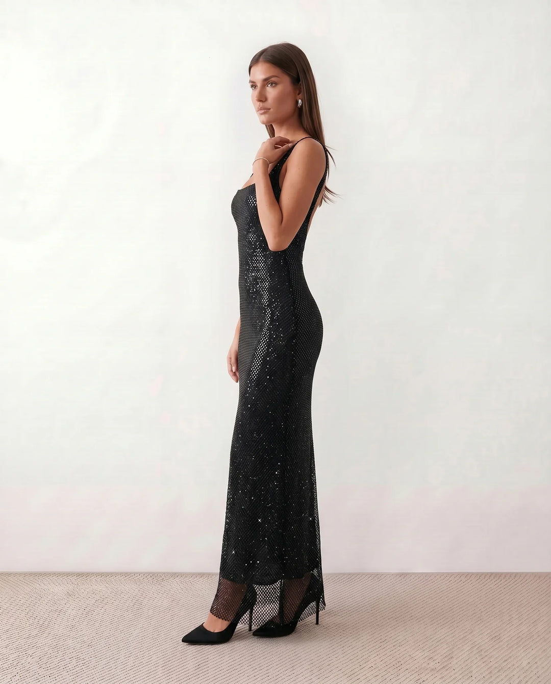 Woman wearing the Mihaela sequined low back maxi dress featuring allover sequin mesh, a square neckline, wide shoulder straps, a low open back, and a fitted floor-length sheath silhouette.