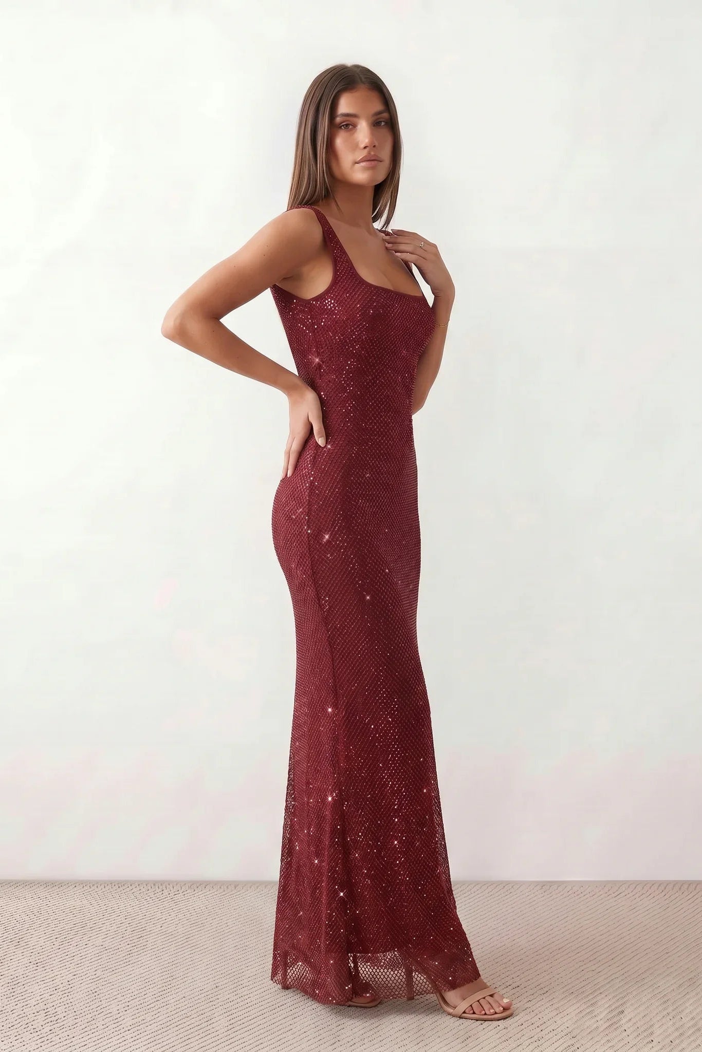 Woman wearing the Mihaela sequined low back maxi dress featuring allover sequin mesh, a square neckline, wide shoulder straps, a low open back, and a fitted floor-length sheath silhouette.