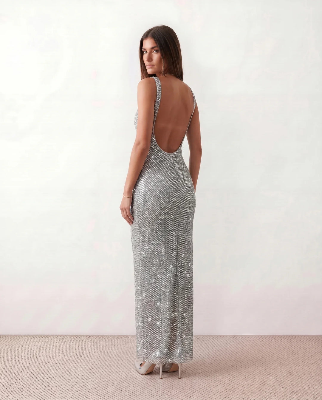 Woman wearing the Mihaela sequined low back maxi dress featuring allover sequin mesh, a square neckline, wide shoulder straps, a low open back, and a fitted floor-length sheath silhouette.