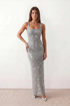 Woman wearing the Mihaela sequined low back maxi dress featuring allover sequin mesh, a square neckline, wide shoulder straps, a low open back, and a fitted floor-length sheath silhouette.