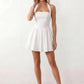 Maren halter backless mini dress with a square halter neckline, corset-seamed bodice, fully open back with tie-neck closure, and a flared A-line mini skirt. Available in black and white.