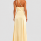 Woman wearing a soft beige asymmetric maxi dress with a one-shoulder neckline, fitted bodice, elegant draped silhouette and thigh-high side split, styled for weddings, evening events and formal occasions.