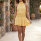 Bella Glossy Halter Mini Dress with a halter mock neckline, tie-back closure, smocked waist, open back, and tiered ruffle mini skirt in a glossy finish, available in Beige, Red, Purple, Yellow, Pink, and Light Blue.